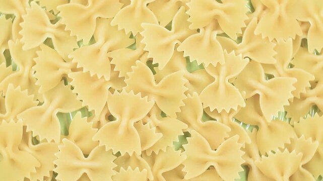 Uncooked Italian Farfalle, butterfly or bow tie pasta, extreme close-up on a green plate, rotating video.