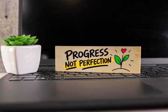 Progress Not Perfection Motivational Quote on Wooden Sign with Laptop and Green Plant Personal Growth and Productivity Concept.