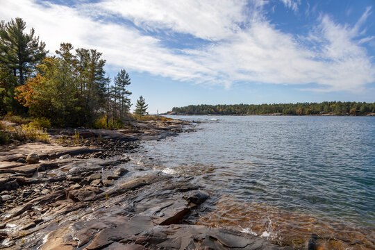 View of Georgian Bay from the rocky shoreline of Lighthouse Trail in Killarney, Ontario, showcasing tranquil waters and lush forests under a clear sky.