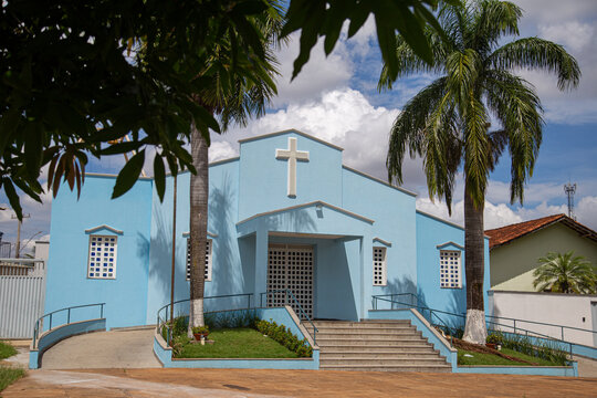Par&oacute;quia Nossa Senhora da Guia vista entre dois coqueiros com c&eacute;u nublado ao fundo.