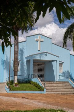 Par&oacute;quia Nossa Senhora da Guia com dois coqueiros na frente e c&eacute;u nublado ao fundo.