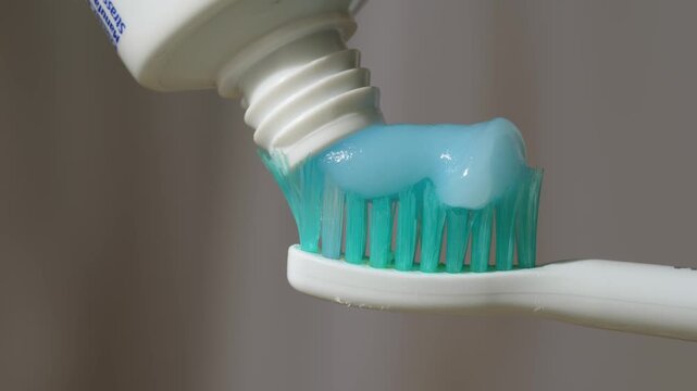 Squeezing blue toothpaste gel onto toothbrush bristles