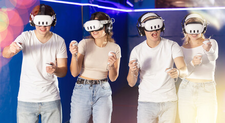 Guys and girls friends experiences effect of being immersed in fictional reality with help of helmet. Gamer manipulate joystick and plays virtual game with companions. E sports competition, new © JackF