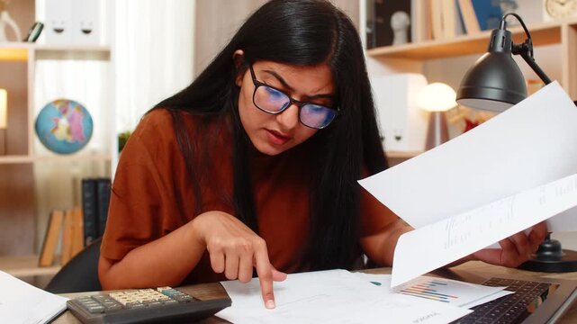 Indian woman on home table finds billing error and checks data with focused attention during budget review. Arabian girl compares figures and verifies records on laptop to solve budget error at home.
