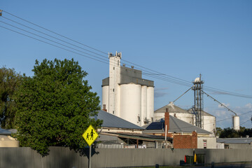 Agricultural grain silos, elevator infrastructure, and metal storage bins looming behind residential homes in the rural township of Keith, South Australia. Grain handling infrastructure © Doublelee