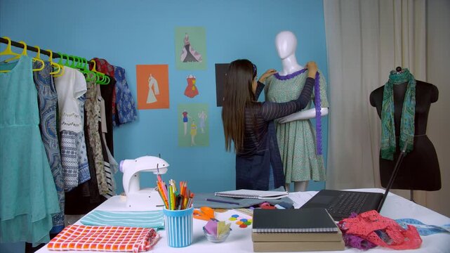 Successful entrepreneur happily working on her upcoming designer dress - Fashion studio. Young fashion designer doing designing work on a dummy and noting down the important details in her laptop 