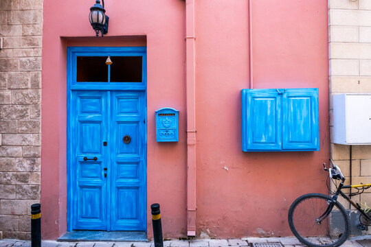A vibrant blue wooden door set against a salmon pink wall on a charming street in the Greek islands, featuring a vintage mailbox and a parked bicycle.