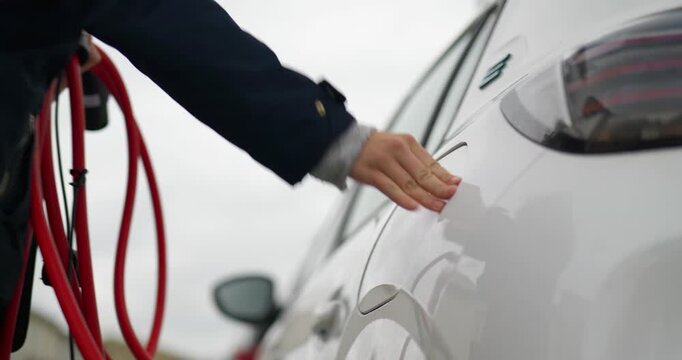 Driver plugging a charging cable into an electric car, close-up