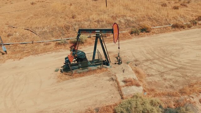 Industrial oil pumping unit beside a dirt road in a remote, arid desert extraction field.