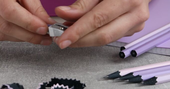 Woman using sharpener at gray textured table, closeup