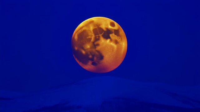Orange moon rising over a snowy ridge