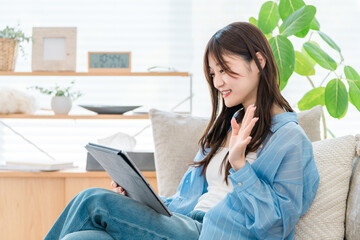 タブレットでビデオ通話をしながら手を振る20代女性。 © buritora