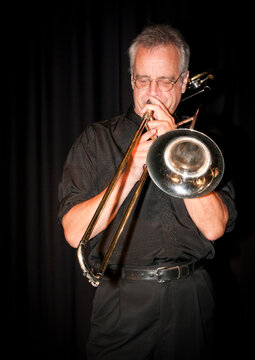 A trombonist playing the trombone against a black background.
