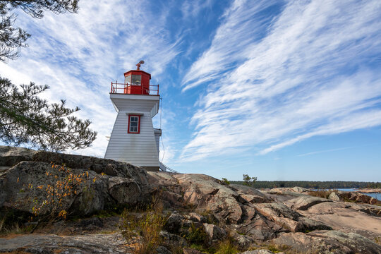 Stunning view of Killarney Lighthouse in Ontario, Canada against a vibrant blue sky, surrounded by rugged rocks and serene natural beauty.