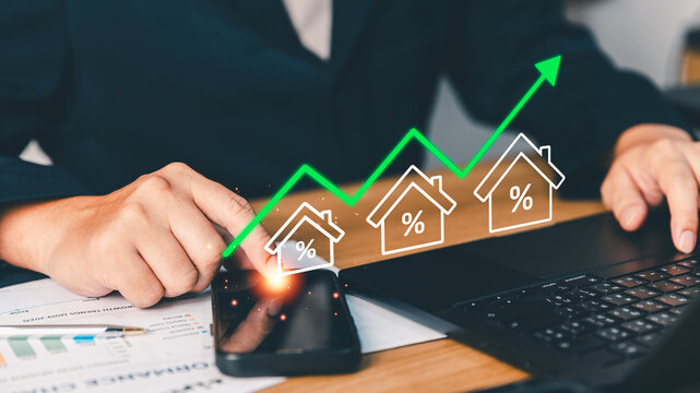 Businessperson analyzing real estate market trends, mortgage interest rates, and housing investment growth using a smartphone and laptop with rising property percentage and upward financial graph