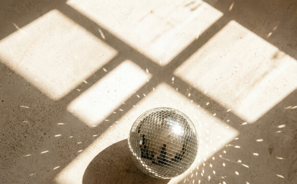 Minimalist aesthetic disco ball on floor with warm sunlight and window shadow patterns