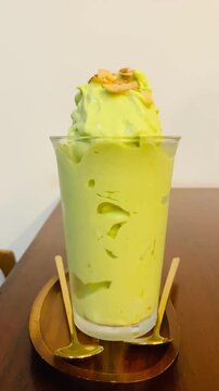 Vertical video of a fresh green avocado smoothie topped with toasted coconut strips served in a glass on a cafe table.