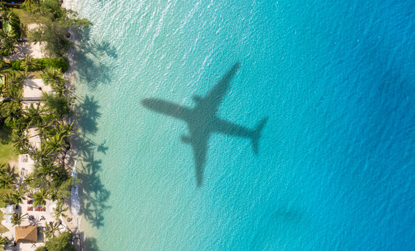 Aerial view of shadow passenger plane silhouette and sandy beach blue sea with waves at sea beach summer vacation sea travel concept	
