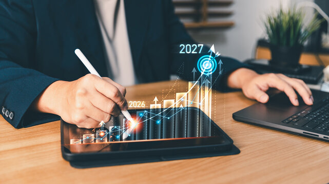 Business planning annual financial growth and business strategy for 2026 and 2027 using a tablet, touching digital target icon and upward charts to analyze corporate performance and investment success