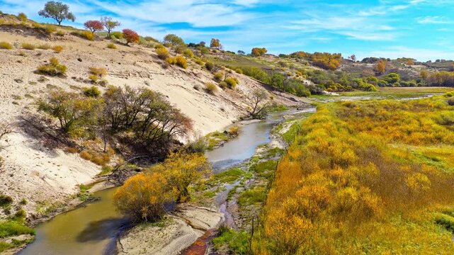 Aerial view of narrow stream flowing past sandy slopes and autumn foliage in Ulan Butong Grassland, Inner Mongolia, China