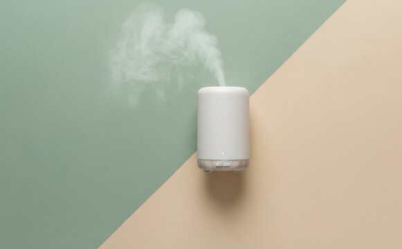 Minimalist white essential oil diffuser releasing fragrant steam on a stylish split green and beige background for aromatherapy