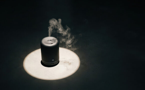 Black essential oil diffuser emitting mist under spotlight in dark room for aromatherapy