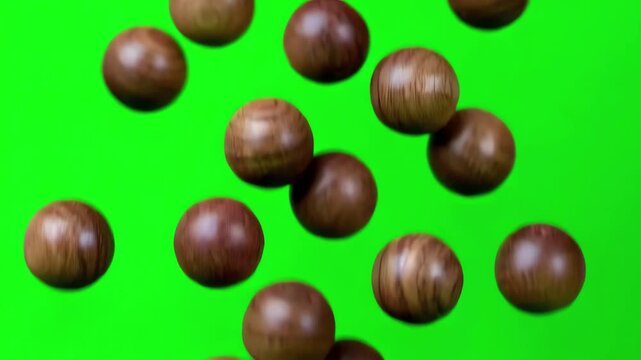 Natural round wooden beads falling in slow motion against a bright green screen background
