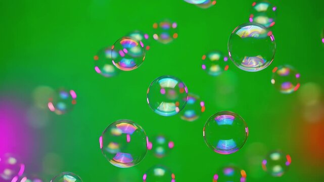 Shimmering iridescent bubbles of various sizes floating upwards against a vibrant green screen background with rainbow light reflections