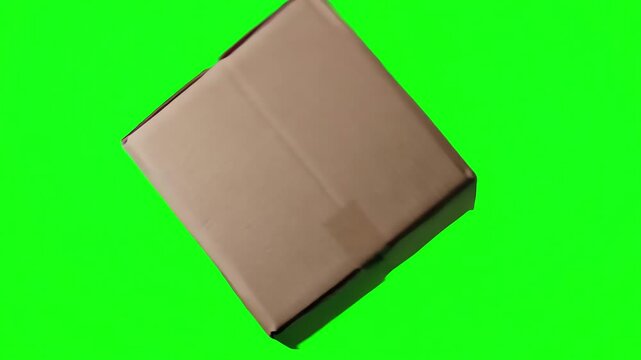 Single blank square cardboard box spinning and tumbling through the air isolated on a green screen background