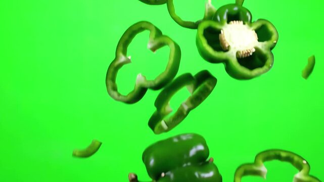 Sliced green bell pepper pieces cascading downwards with a spinning motion isolated on a vivid green screen studio background