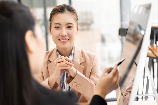 Asian Businesswoman Smiling and Listening to Colleague Explaining Data on Computer Screen