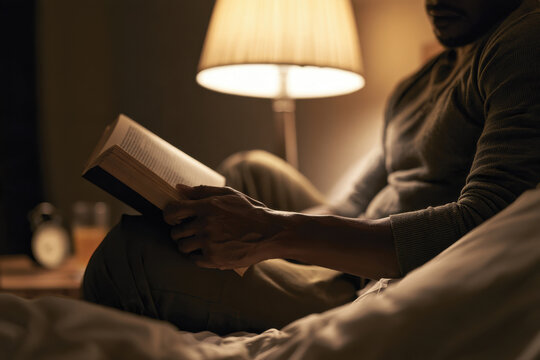 A man indulges in a book while reclining in bed, surrounded by a warm ambiance and soft lighting, creating an intimate and cozy atmosphere that invites relaxation and escape.