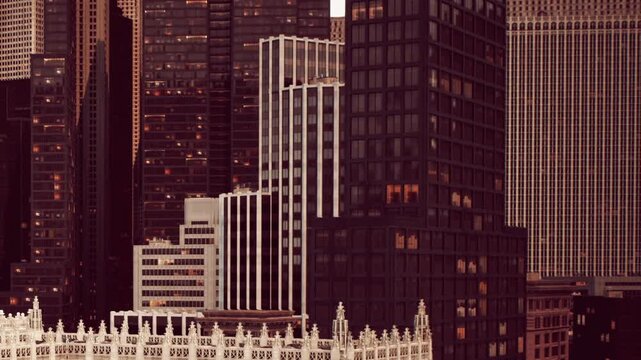 Tall modern skyscrapers stand close together in city center with glowing windows lighting up during evening hour