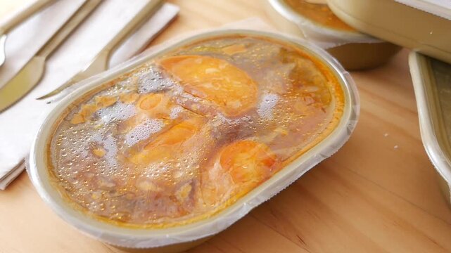 Plastic takeaway container holds broth with orange food pieces on a wooden table