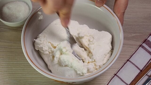 Soft cottage cheese curd is kneaded with a fork in a plate. Fermented milk products, closeup.