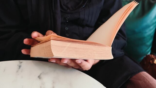 Hands holding an open book while seated at a table
