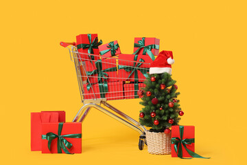 Holiday shopping and consumerism, shopping cart filled with red gift boxes and decorated christmas tree on a yellow background © Pixel-Shot