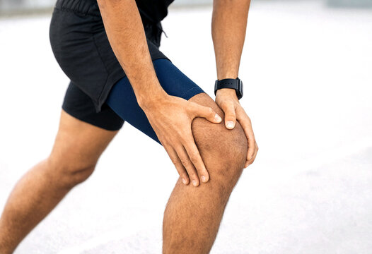 Person holding knee while experiencing discomfort during outdoor physical activity or sports training