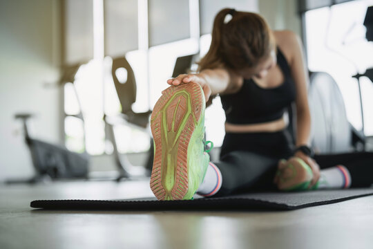 Woman in sportswear doing seated hamstring stretch on exercise mat in bright gym with natural light