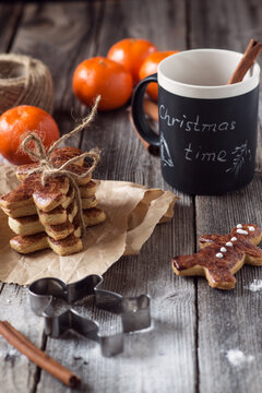 Close-up of a stack of homemade Christmas gingerbread man cookies on a rustic wooden table with a cookie cutter, satsumas, cinnamon sticks and a mug with the words christmas time