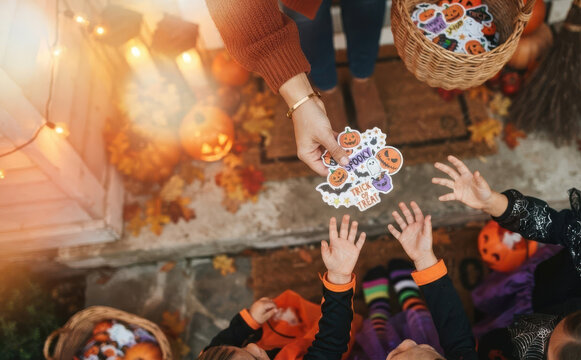 Adult giving Halloween stickers to children in costumes during trick or treat festivities outdoors at doorstep