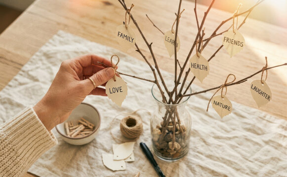 Woman making gratitude tree craft project with paper leaves on branches in glass vase on table top view