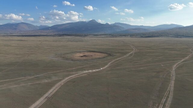 Wide aerial drone perspective tracking a lonely unpaved road stretching parallel to the shoreline of the expansive Khoton Nuur Lake in Tavan Bogd National Park, Mongolia