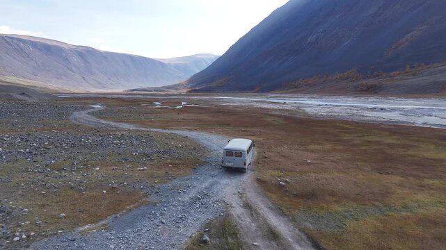 Aerial drone perspective following a single vehicle traveling along a dusty dirt track running parallel to the White Milky River in Tavan Bogd National Park, Mongolia