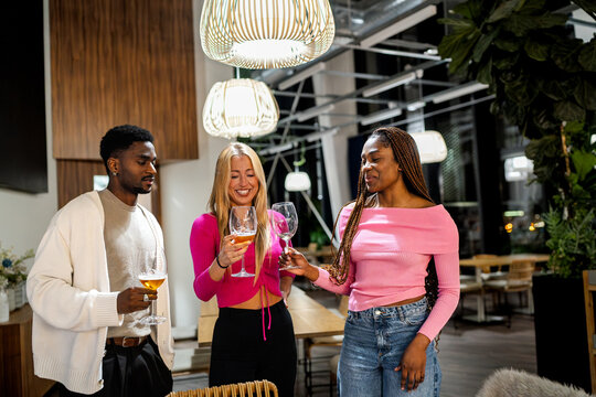 Three friends celebrating and socializing during a night out at a modern restaurant, clinking glasses and having fun
