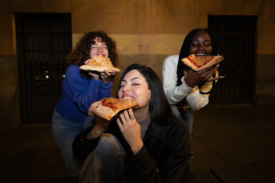 Friends enjoying pepperoni pizza slices outdoors at night