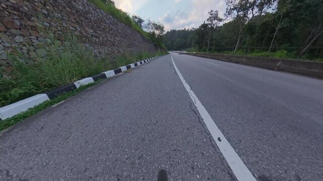 Horizontal cycling POV footage along a winding mountain road, passing a stone retaining wall, black and white curb markings and a pickup truck ahead on the asphalt road.