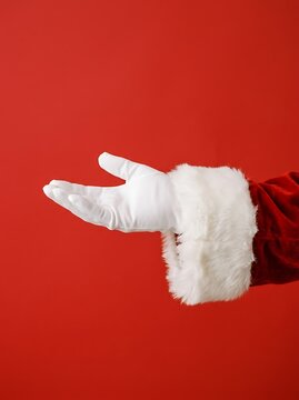 Santa claus hand wearing a white glove reaching out against a solid red background, festive holiday gesture for christmas greeting