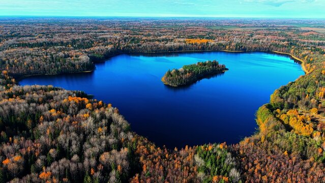 Aerial view of a serene lake surrounded by vibrant autumn forest colors reflecting on water