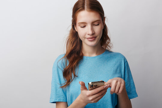 Mobile software tester, young woman looking focused at her smartphone screen, tapping carefully. A clean white background highlights her concentration and digital device interaction.